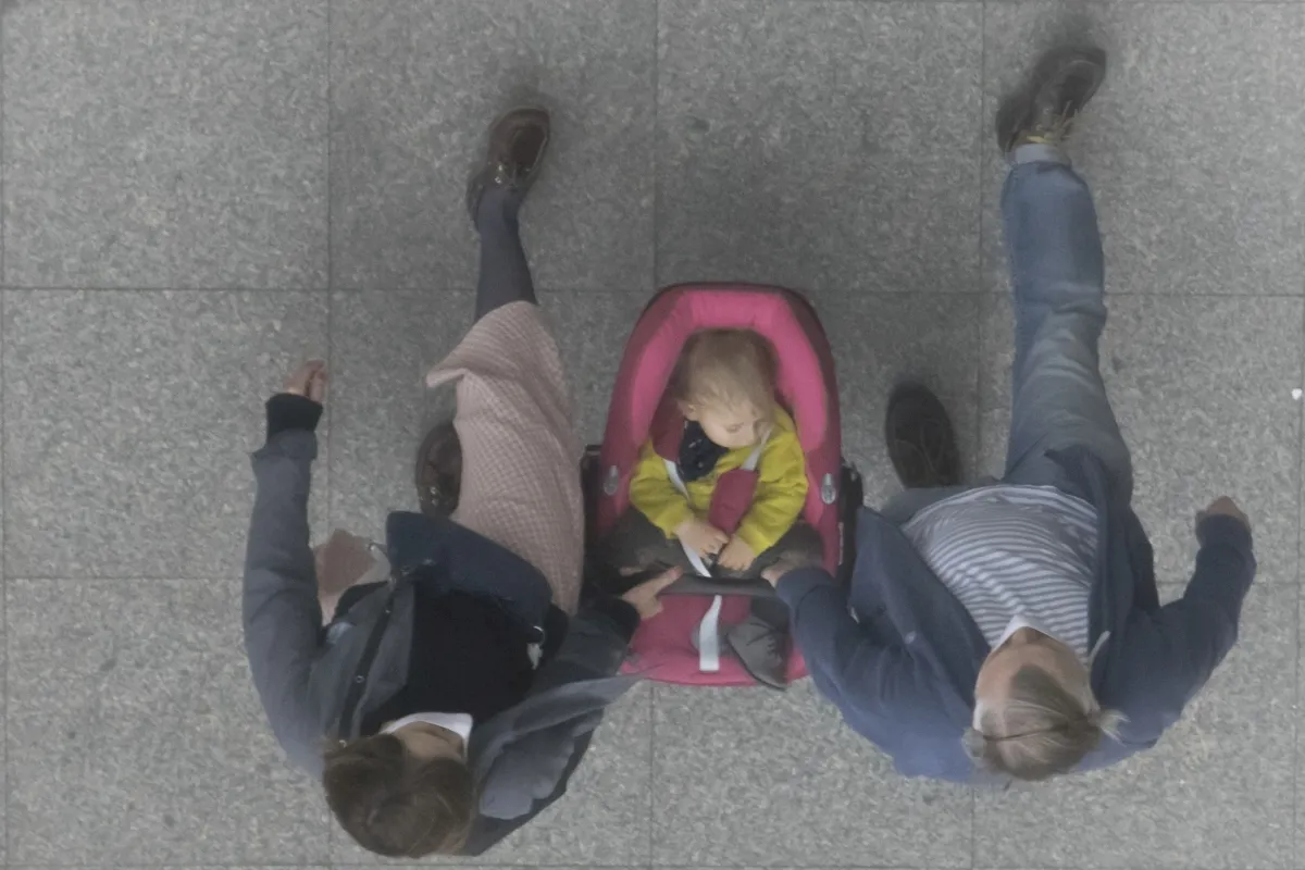 Two adults walking on either side of a child in a pink stroller seen from above